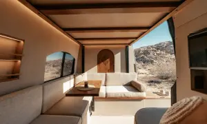 Gemütlicher wohnmobil innen mit Sitzbank, Tisch und Holztür. Blick auf Wüstenlandschaft.