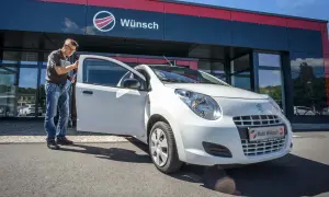 Mann prüft einen weißen Suzuki Alto vor dem Autohaus Wunsch. Mögliche Suzuki Alto Probleme werden hier behoben.