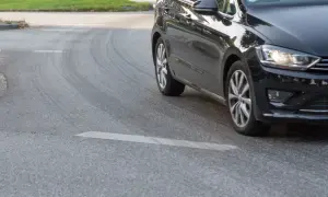 Schwarzes Auto fährt eine Kurve, die Reifen quietschen beim Beschleunigen.