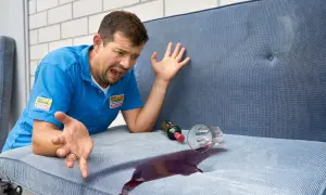 Mann mit verzweifeltem Gesichtsausdruck, der versucht, Rotwein auf einem Wohnwagenpolster zu reinigen.