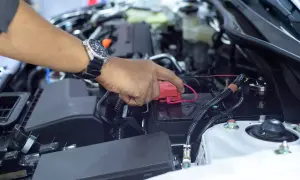 Hand mit Uhr lädt die Autobatterie ohne Abklemmen. Roter Stecker wird auf den Pluspol gesetzt.