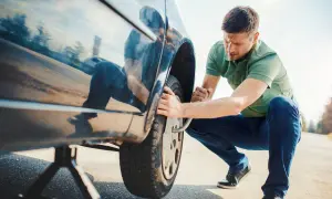 Mann wechselt Reifen am Auto. Der Wagen steht auf einem Wagenheber, während er die Radmuttern löst.