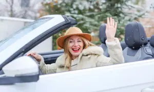 Fröhliche Frau winkt aus einem weißen Cabrio im Winter, während Schneeflocken fallen.