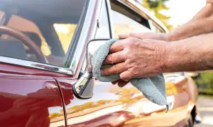 Hände polieren den roten Oldtimer mit einem Mikrofasertuch. So kann das Auto wachsen ohne polieren, für einen glänzenden Auftritt.