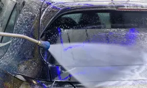 Ein Hochdruckreiniger spritzt Schaum auf ein schwarzes Auto. Die richtige auto waschen reihenfolge sorgt für Glanz.