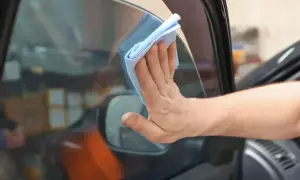 Hand wischt mit blauem Tuch die Windschutzscheibe innen reinigen streifenfrei.