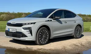 Grauer Skoda Enyaq Coupé auf staubiger Straße, umgeben von grünen Feldern. Manche Fahrer berichten von Skoda Enyaq Problemen, aber dieses Modell scheint unbeeindruckt.