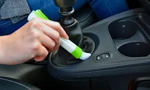 Hand reinigt mit Bürste den Bereich um den Schalthebel, um Staub im Auto zu entfernen.