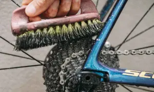 Mit Hausmitteln die Fahrradkette reinigen: Eine Bürste schrubbt die Kette und Kassette des glänzenden blauen Fahrradrahmens.