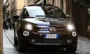 Dunkelbrauner Fiat 500 mit leuchtenden Scheinwerfern auf einer Kopfsteinpflasterstraße. Ein paar Leute gehen im Hintergrund vorbei. Keine sichtbaren Fiat 500 Probleme.