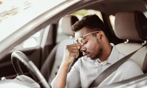 Mann im Auto mit Kopfschmerzen, fragt sich, darf man mit Antidepressiva Autofahren?