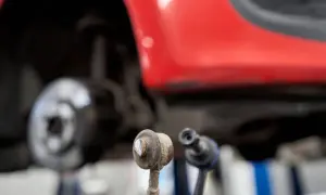 Zwei Koppelstangen liegen vor einem roten Auto. Eine Koppelstange ist defekt und muss ersetzt werden.