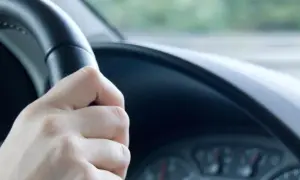 Hand am Lenkrad, das leicht flattert. Die Straße zieht vorbei, ein Gefühl von Bewegung.