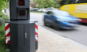 Ein Blitzer-Foto zeigt ein schnelles Auto, das vorbeifährt, während ein gelber Bus im Hintergrund verschwimmt.