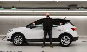 Mann neben weißem Seat Arona in Tiefgarage, lächelnd mit ausgestreckten Armen. Keine Seat Arona Probleme hier.