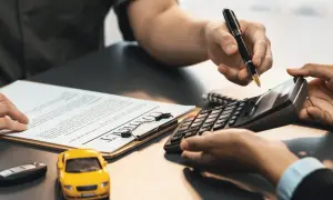 Hände mit Stift und Taschenrechner über einem Vertrag. Ein gelbes Spielzeugauto und ein Autoschlüssel liegen daneben. Hier wird besprochen, ob Autoreparatur steuerlich absetzbar ist.
