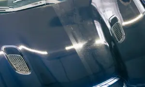 Dunkelblaue Motorhaube mit Lüftungsgittern, zeigt deutliche Swirls und Kratzer. Die Kosten für Motorhaube polieren sind hier sichtbar.