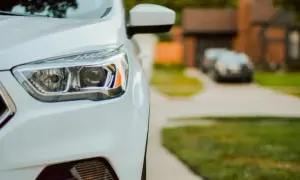 Nahaufnahme eines weißen Autos, Scheinwerfer polieren für klare Sicht. Im Hintergrund ein Haus und ein weiteres Auto.