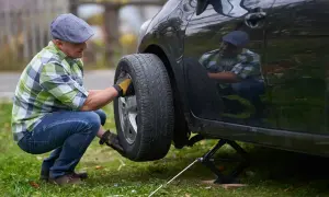 Mann wechselt Reifen mit Reifendrucksensor. Er kniet neben dem Auto, das auf einem Wagenheber steht.