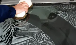 Hand reinigt mit Schwamm und Schaum die Autoscheiben.