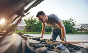 Mann beugt sich über den Motorraum, weil der auto riecht nach benzin. Die Sonne scheint.