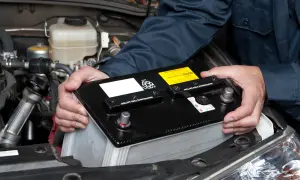 Hände halten eine Autobatterie, um sie aus dem Motorraum zu entfernen. Das **batterie abklemmen** ist ein wichtiger Schritt bei der Wartung.
