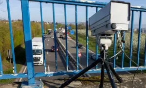Ein Monocam Blitzer auf einem Stativ überwacht den Verkehr auf einer Autobahn. Autos und Lastwagen fahren auf der mehrspurigen Straße.