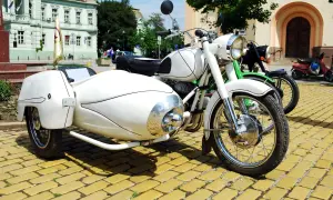 Weiße Motorräder mit Beiwagen und Roller stehen auf einem gelben Kopfsteinpflaster. Ein Helm liegt auf dem Roller, um die Strafe für Fahren ohne Helm zu vermeiden.