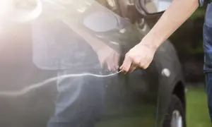 Hand mit Schlüssel verursacht Mikrokratzer am Auto. Die Sonne reflektiert auf dem dunklen Lack.