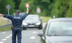 Polizist regelt den Verkehr bei einer allgemeinen Verkehrskontrolle. Er hält ein Stoppschild hoch und winkt Autos weiter.