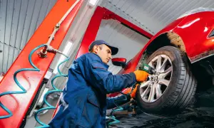 Mechaniker wechselt Reifen am roten Auto. Die Frage "wie lange dauert reifenwechsel" wird hier beantwortet: schnell und effizient.