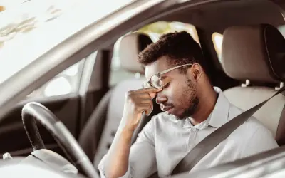 Mann im Auto mit Kopfschmerzen, fragt sich, darf man mit Antidepressiva Autofahren?