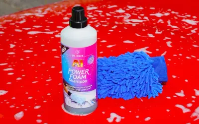 Flasche "A1 Power Foam Shampoo" und blauer Waschhandschuh auf rotem, seifigem Autolack. So gelingt das auto waschen ohne autoshampoo.