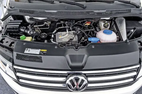 VW T6 150 PS Motorraum mit sichtbaren Leitungen und Kühlmittelbehälter. Mögliche Probleme am Motor sind hier zu sehen.