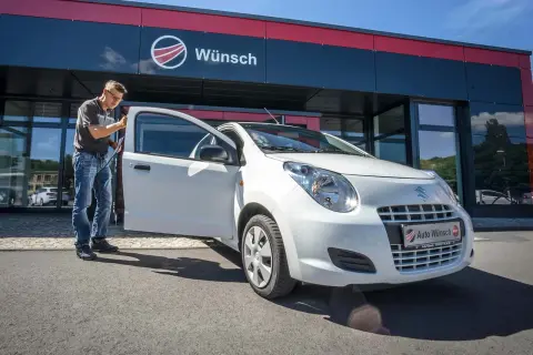 Mann prüft einen weißen Suzuki Alto vor dem Autohaus Wunsch. Mögliche Suzuki Alto Probleme werden hier behoben.