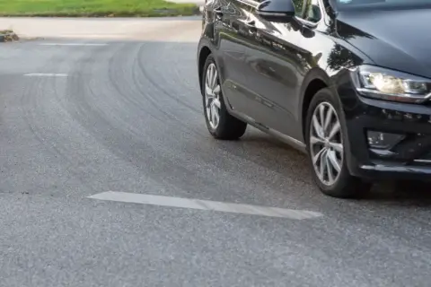 Schwarzes Auto fährt eine Kurve, die Reifen quietschen beim Beschleunigen.