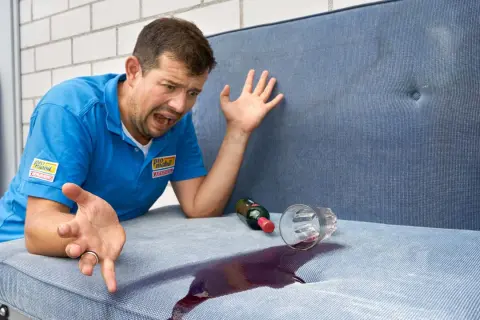 Mann mit verzweifeltem Gesichtsausdruck, der versucht, Rotwein auf einem Wohnwagenpolster zu reinigen.