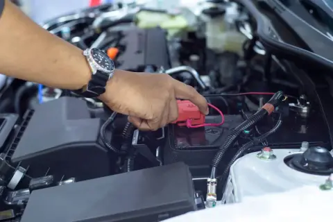 Hand mit Uhr lädt die Autobatterie ohne Abklemmen. Roter Stecker wird auf den Pluspol gesetzt.