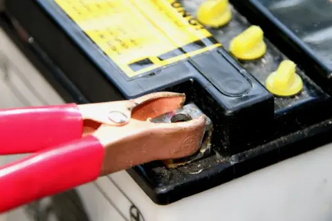 Rote Klemme verbindet sich mit einem Batteriepol, um eine tiefentladene Batterie wieder aufzuladen.