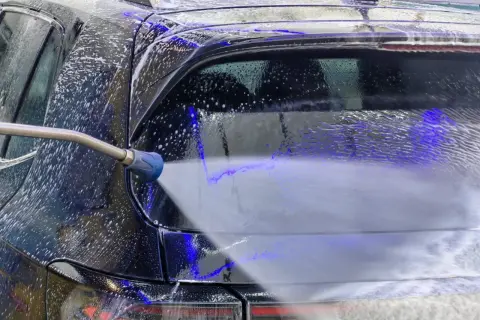Ein Hochdruckreiniger spritzt Schaum auf ein schwarzes Auto. Die richtige auto waschen reihenfolge sorgt für Glanz.