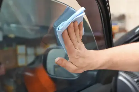 Hand wischt mit blauem Tuch die Windschutzscheibe innen reinigen streifenfrei.