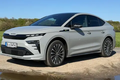 Grauer Skoda Enyaq Coupé auf staubiger Straße, umgeben von grünen Feldern. Manche Fahrer berichten von Skoda Enyaq Problemen, aber dieses Modell scheint unbeeindruckt.