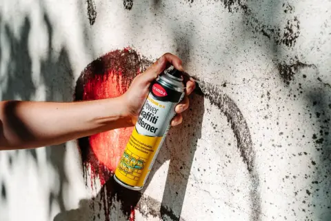 Hand hält Sprühdose mit Graffiti-Entferner. Ideal, um Graffiti von Wänden zu entfernen, fast wie felgenreiniger selber machen.