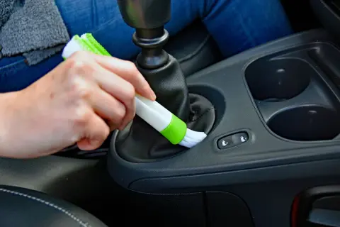 Hand reinigt mit Bürste den Bereich um den Schalthebel, um Staub im Auto zu entfernen.