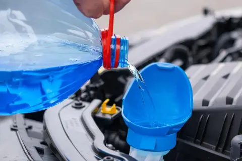 Blauer Scheibenreiniger wird aus einer Flasche in den Einfüllstutzen gegossen. Perfekt für das Scheibenwischwasser Sommer selber machen.