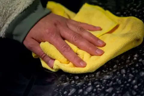 Hand poliert mit gelbem Tuch den dunklen Lack, um das Auto zu polieren und versiegeln.