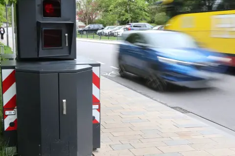 Ein Blitzer-Foto zeigt ein schnelles Auto, das vorbeifährt, während ein gelber Bus im Hintergrund verschwimmt.