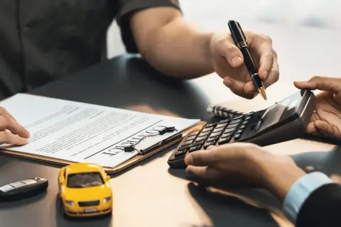 Hände mit Stift und Taschenrechner über einem Vertrag. Ein gelbes Spielzeugauto und ein Autoschlüssel liegen daneben. Hier wird besprochen, ob Autoreparatur steuerlich absetzbar ist.