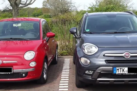Zwei Fiat 500X, rot und grau, parken nebeneinander. Der graue hat ein paar kleine Probleme, die man auf den ersten Blick nicht sieht.
