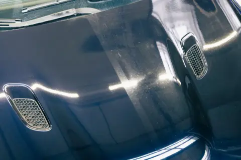 Dunkelblaue Motorhaube mit Lüftungsgittern, zeigt deutliche Swirls und Kratzer. Die Kosten für Motorhaube polieren sind hier sichtbar.